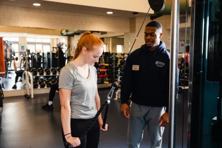 A student trainer assists another student in a fitness center. 