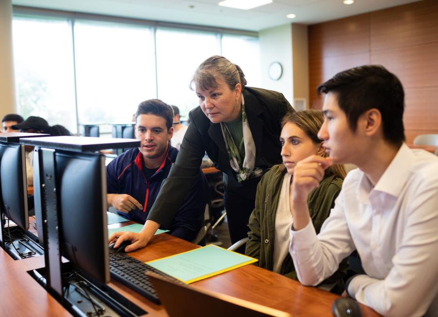 students and professor looking at computer screens in the classroom