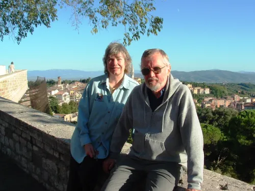 A man and woman in a tourist photo with a medieval Italian landscape behind them.
